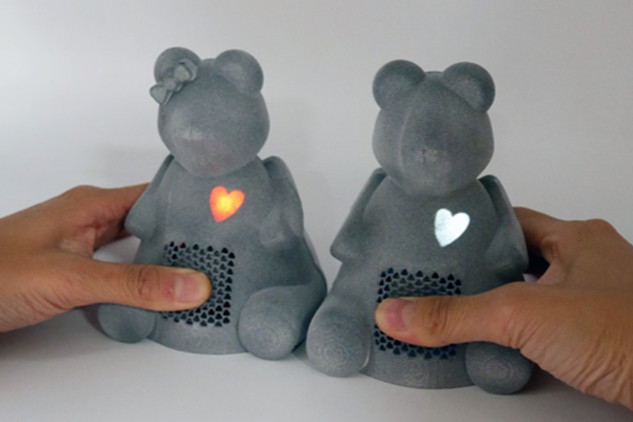 Two 3D printed bears with a soft belly. A finger is pressing on  one of them and a heart lights up from inside the bear.